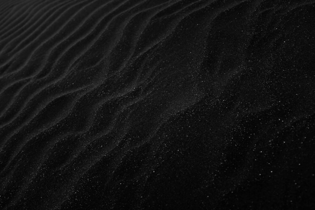 Textured black sand with ripples resembling dunes, creating a dark, abstract aesthetic.
